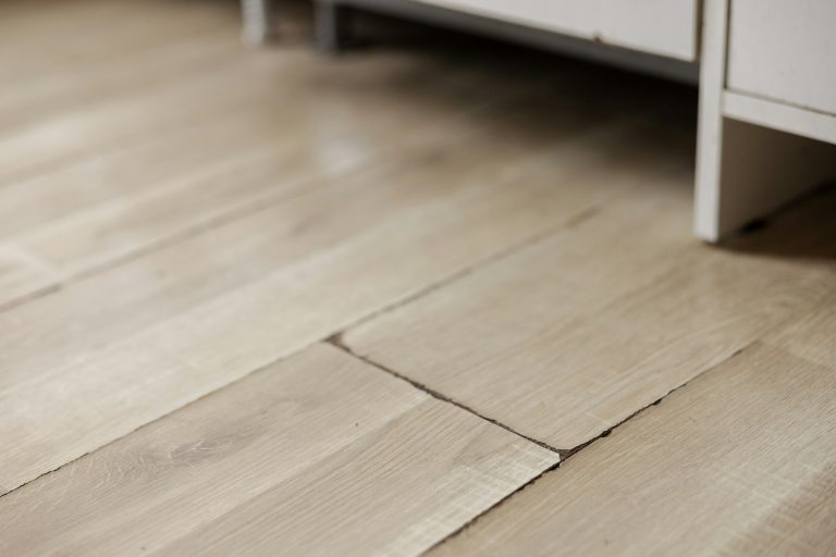 Swollen and dirty laminate floor, close up view. Moisture damage. Laminate flooring has swelled